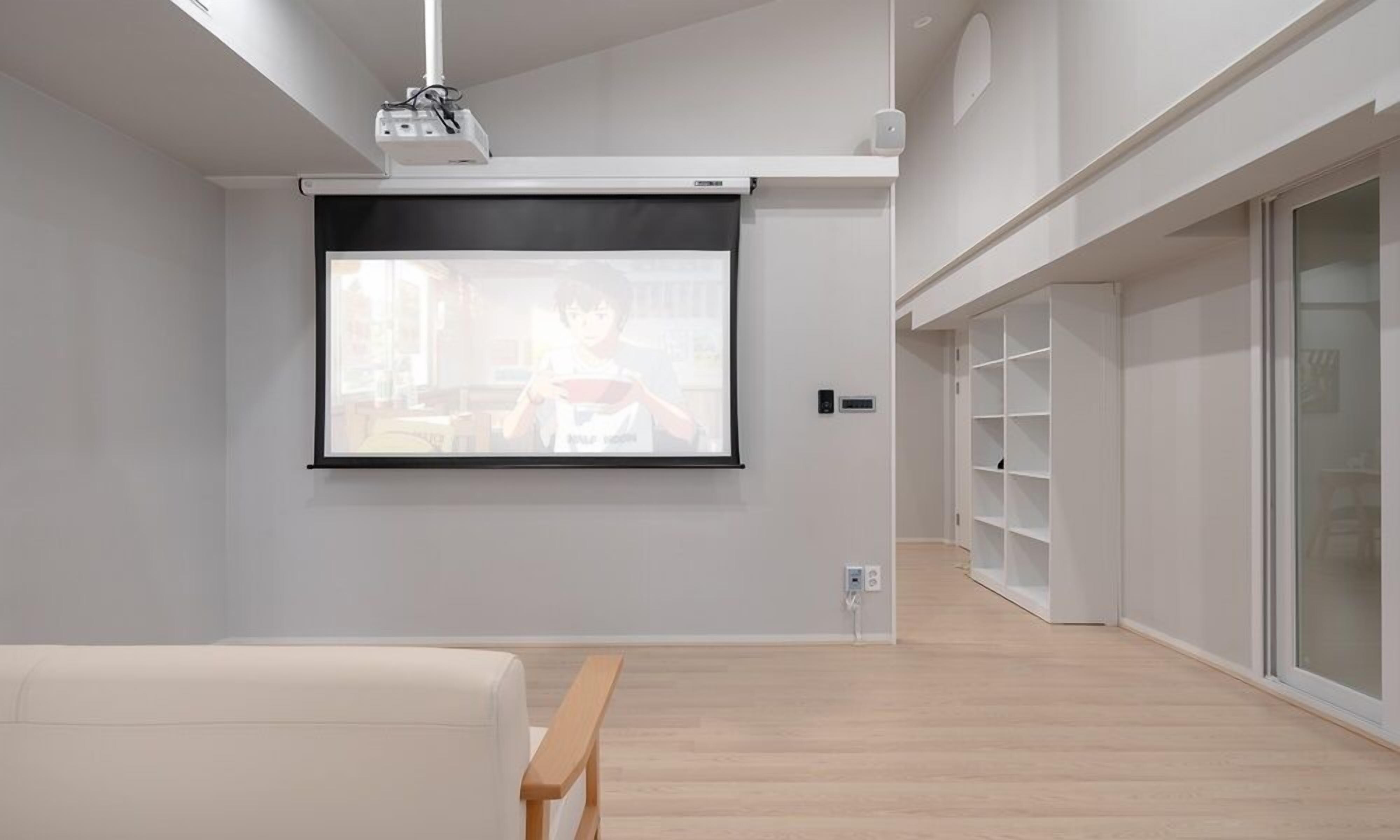 A modern room with a projector screen, a white sofa, a wooden bench, and a built-in shelving unit.