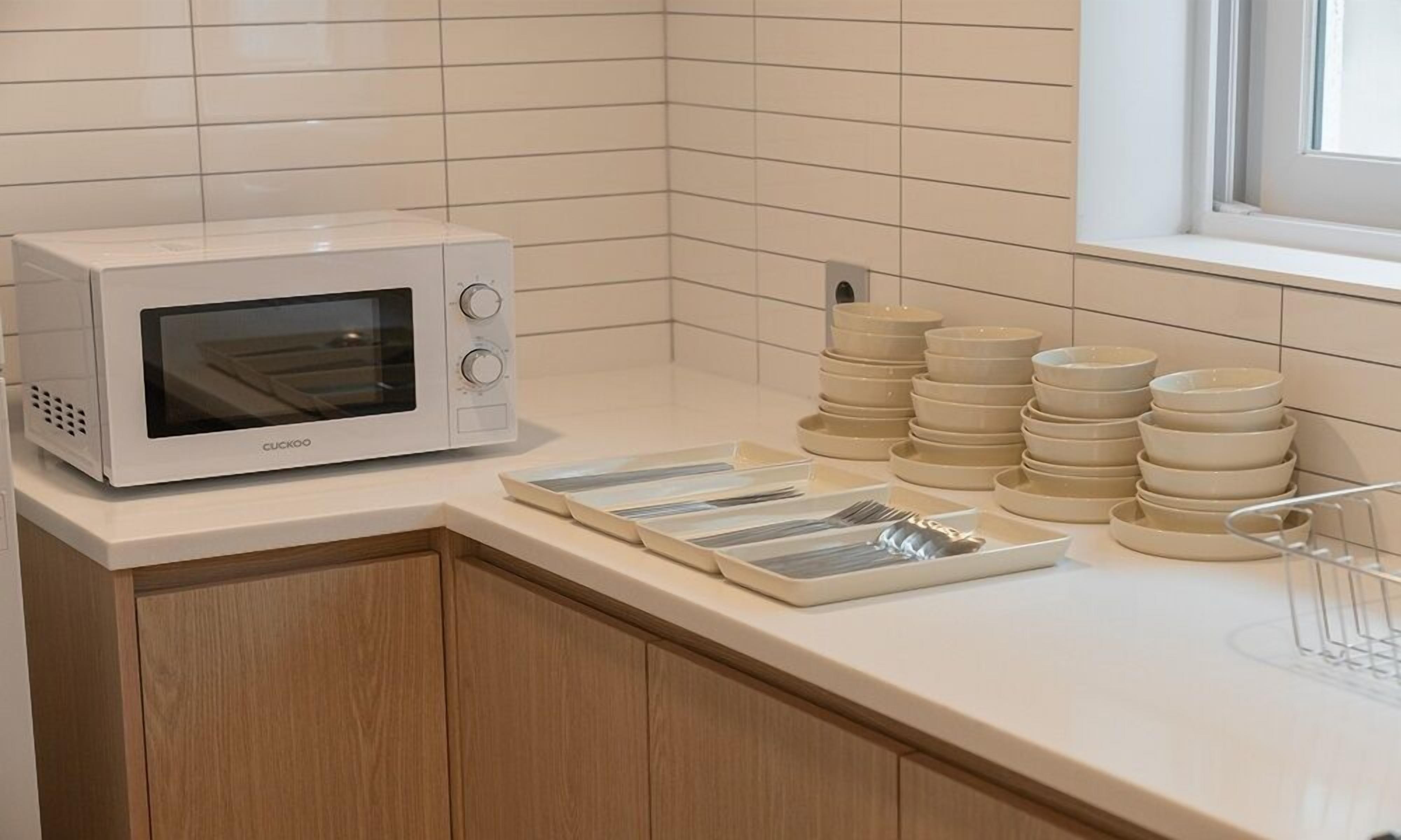 Una cocina con un microondas blanco, cuencos apilados y un ventanal.
