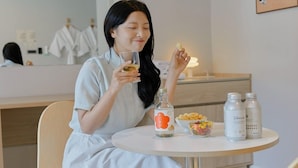 A person sitting at a table with a bottle of water, a bowl of snacks, and two bottles of lotion. - ANNK HOTEL CHEONAN SEONGJEONG (Cheonan)