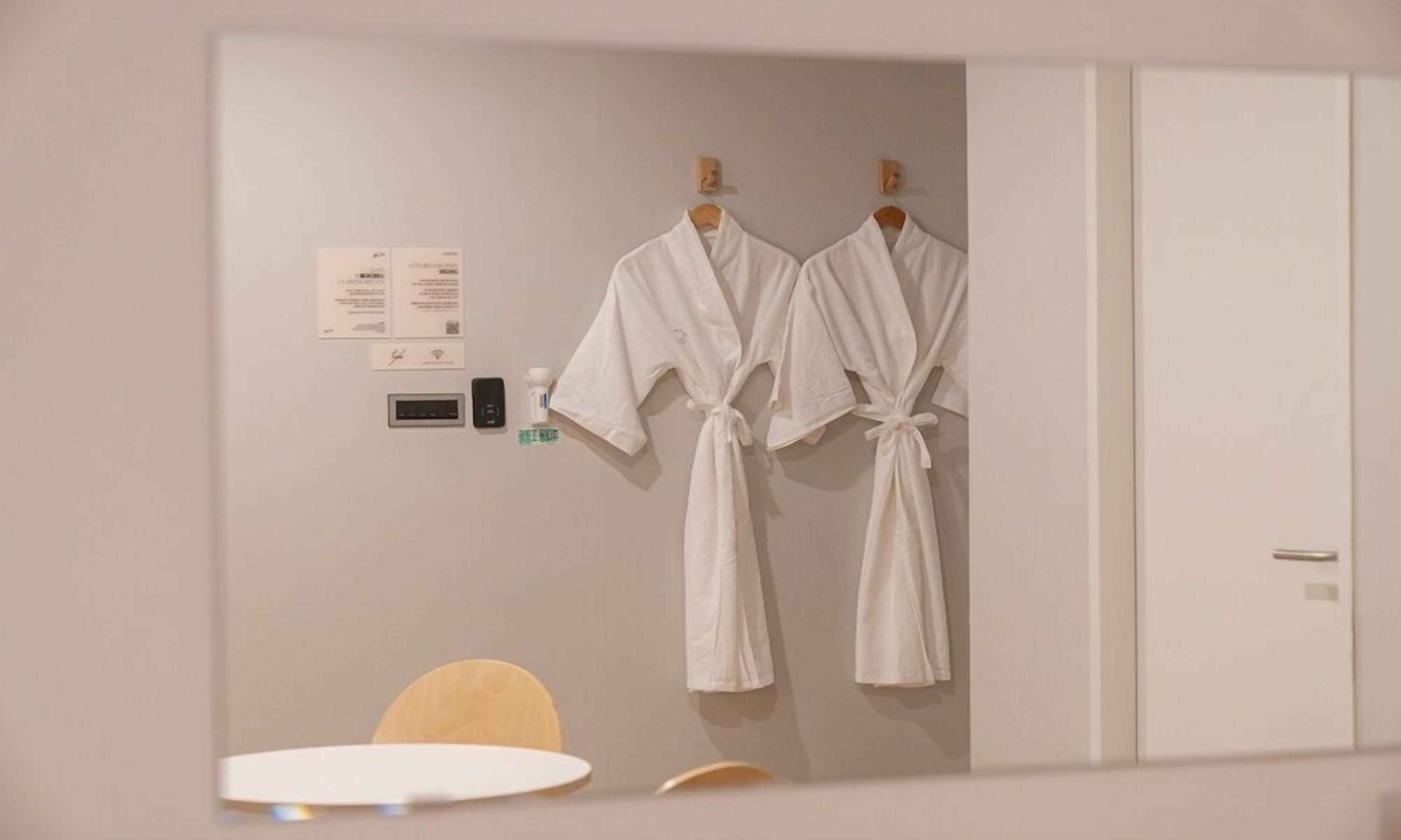 A hotel room with two white robes hanging on a wall, a small table, and a cabinet.