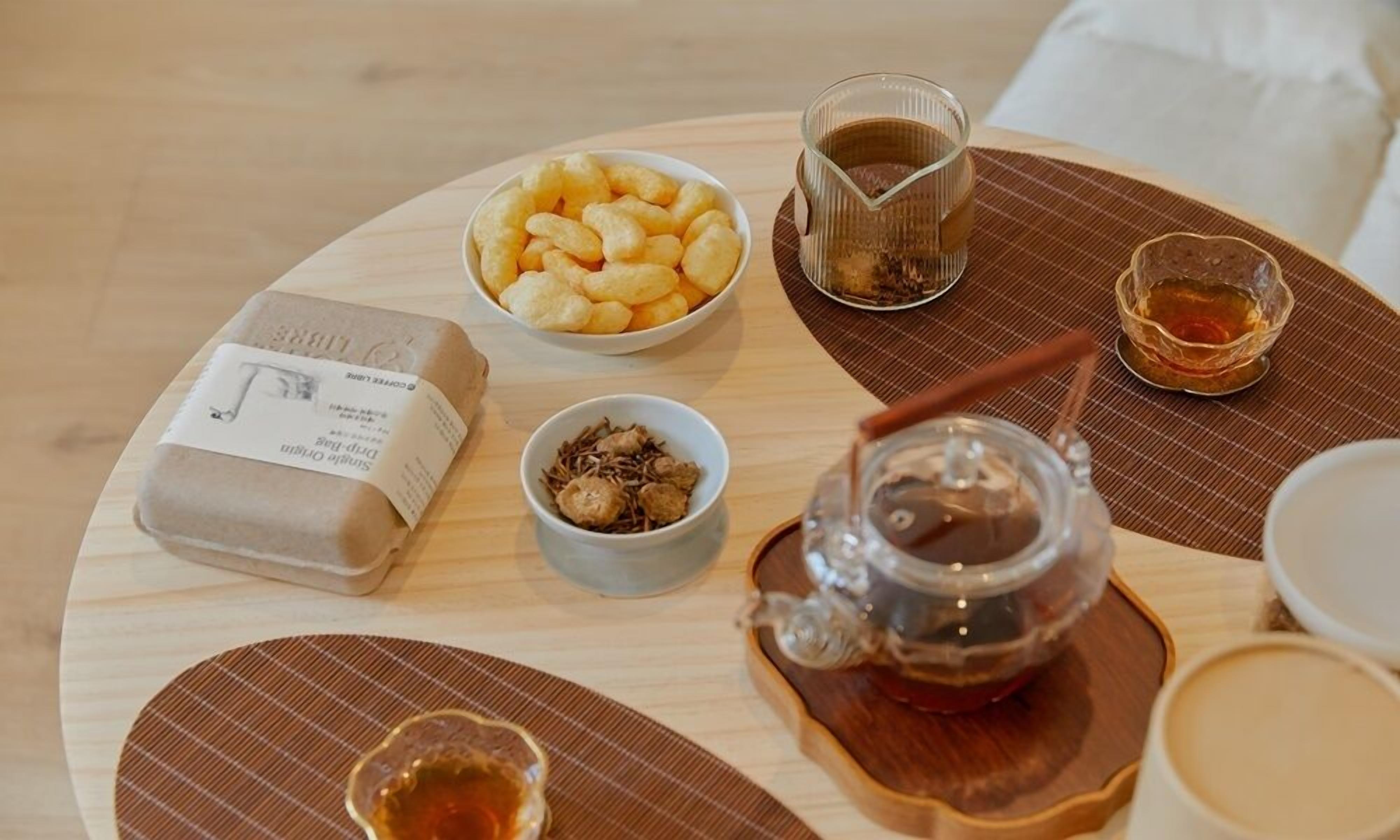 Een ronde houten tafel met diverse spullen, waaronder een schaal met hapjes, een kop thee, een klein schaaltje gedroogde ingrediënten en een pot honing.