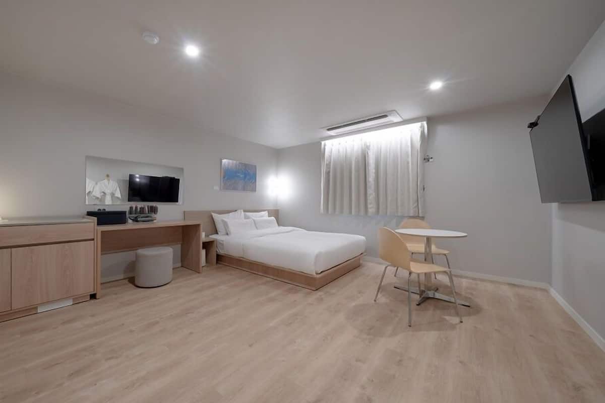 A modern hotel room with a bed, a desk, a chair, and a TV.