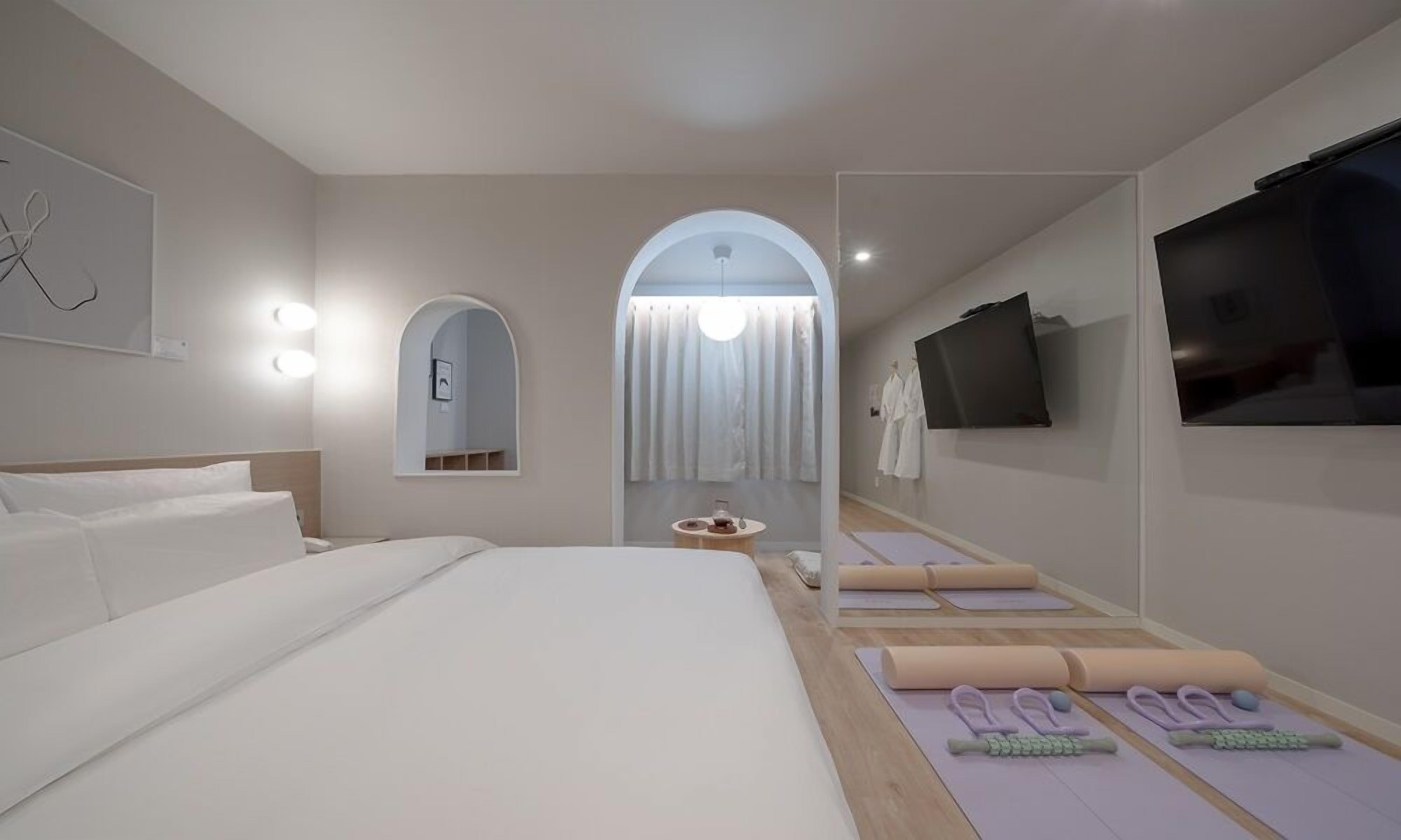 Una habitación de hotel moderna con una cama grande, un televisor, un espejo y colchonetas de ejercicio.