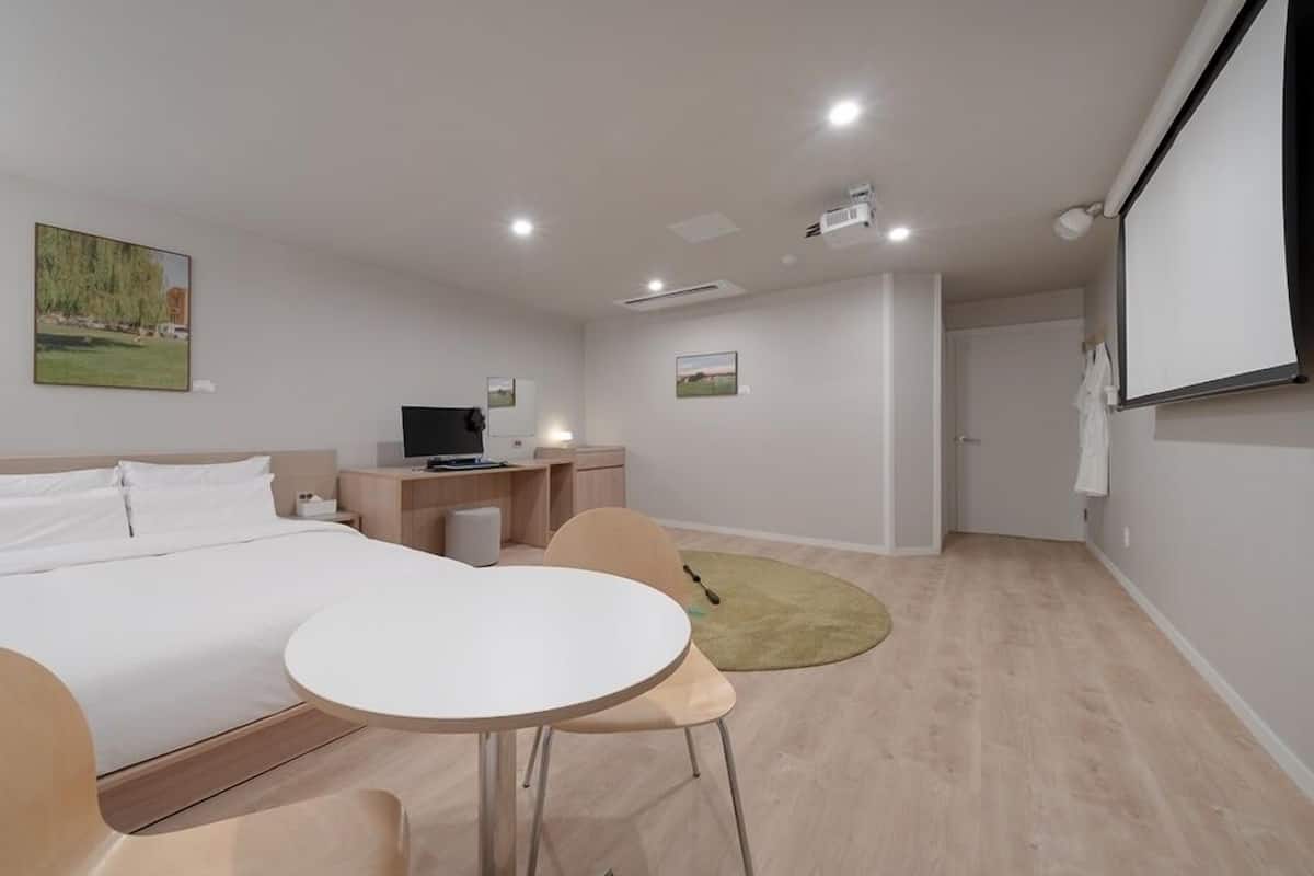 A modern hotel room with a bed, a desk, a chair, and a small table.
