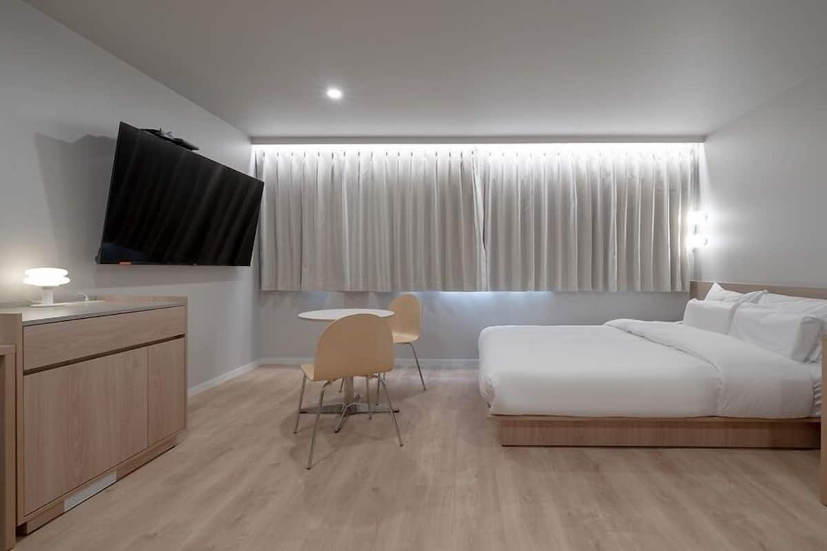 A modern hotel room with a bed, a desk, a chair, and a TV mounted on the wall.