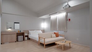 A modern hotel room with a bed, a sofa, a coffee table, a desk with a lamp, and a projector. - ANNK HOTEL CHEONAN SEONGJEONG (Cheonan)