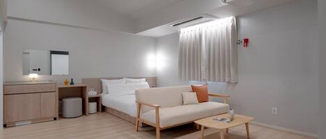 Habitación de hotel moderna con cama, sofá, mesita de centro, escritorio con lámpara y proyector.