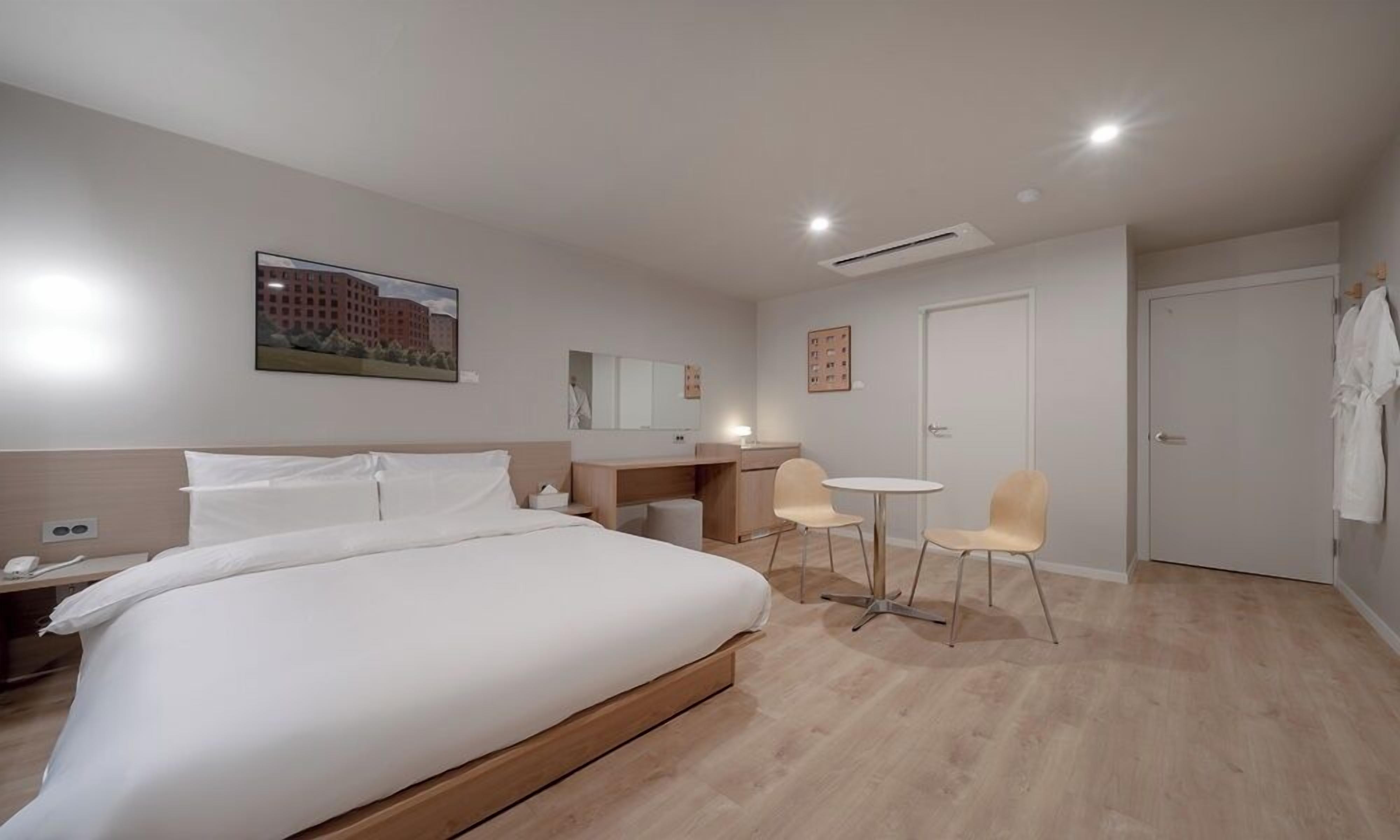 Una habitación de hotel con cama, escritorio, dos sillas, espejo y puerta.