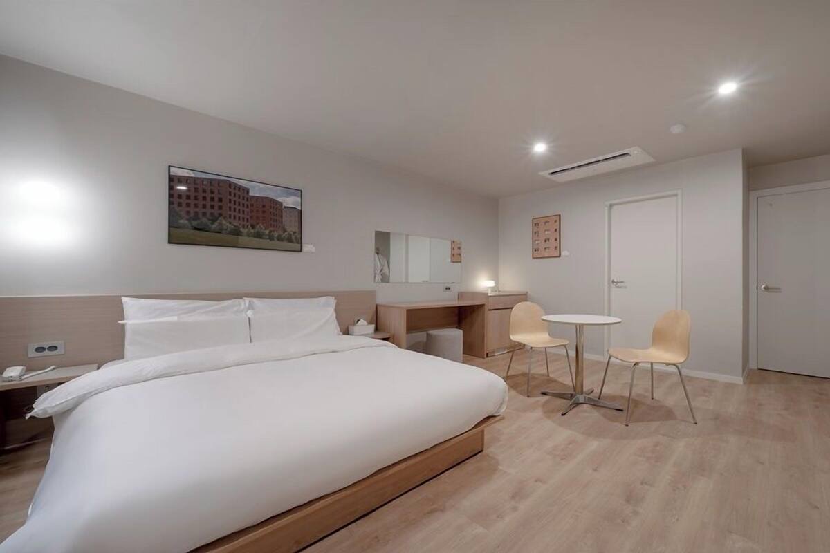 A hotel room with a bed, a desk, two chairs, a mirror, and a door.