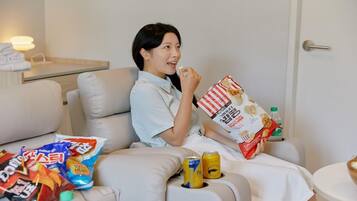A person sitting on a bed with snacks and drinks.