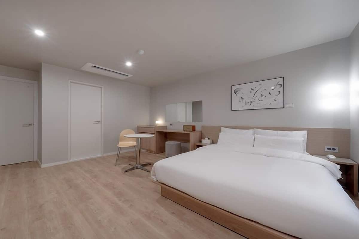 A modern hotel room with a large bed, a desk, a chair, and a small table.