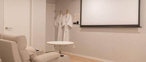A modern room with a massage chair, a small round table, and a projector screen on the wall.