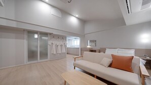 A modern hotel room with a sofa, a bench, and a sliding glass door leading to a bathroom with robes hanging. - ANNK HOTEL CHEONAN SEONGJEONG (Cheonan)