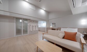 Una habitación de hotel moderna con un sofá, una banca y una puerta corrediza de vidrio que da a un baño con batas colgadas.