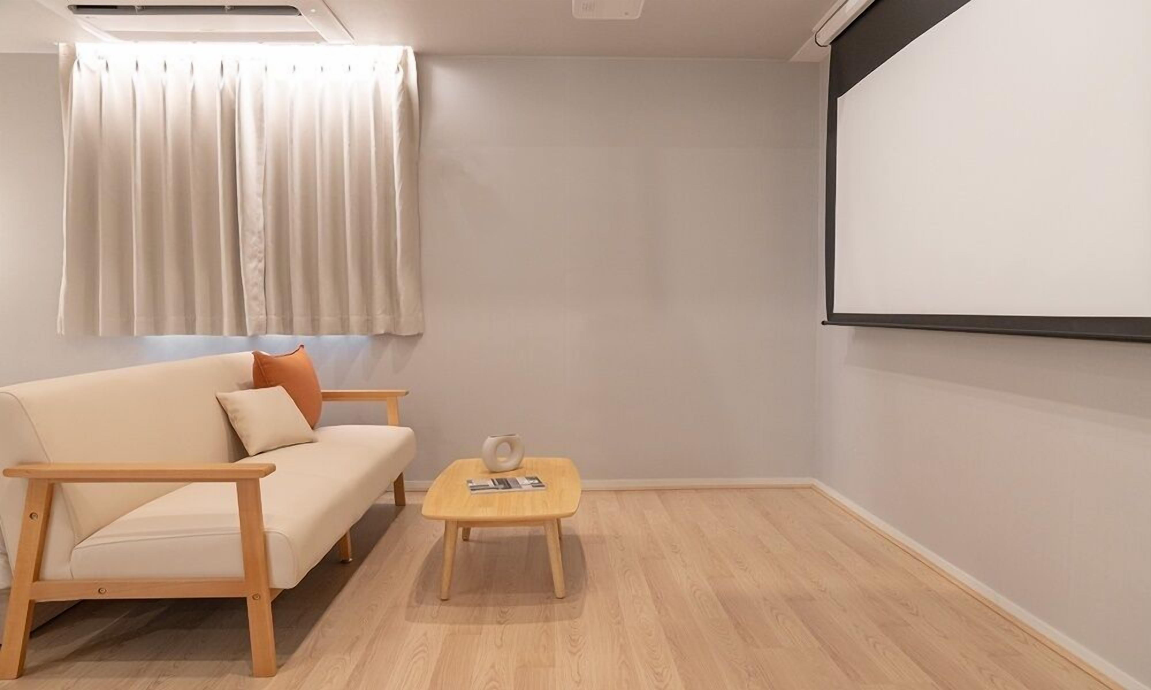 A minimalist living room with a sofa, a coffee table, and a projector screen.