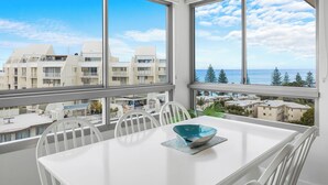 A balcony with a white table and chairs, a blue bowl, and a view of buildings and trees. - Nova Ocean Views Mooloolaba 2 Bedroom Apartment (Sunshine Coast)