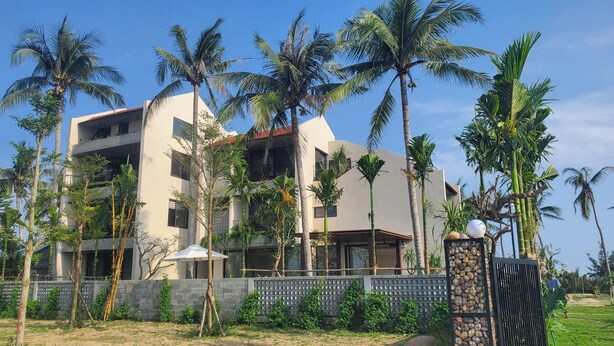 A multi-story building with balconies, surrounded by palm trees and a stone wall. - Apartment for 2 people on 1st floor with 1 room and 1 bathroom -Hoi An Lifestyle (Hội An)