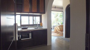 A kitchen with dark cabinetry, a microwave, and a window. There is a doorway leading to a balcony with a wicker chair. - Apartment for 2 people on 1st floor with 1 room and 1 bathroom -Hoi An Lifestyle (Hội An)