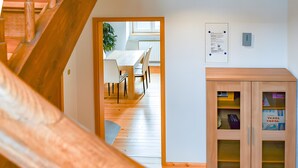 Een houten trap die leidt naar een eetruimte met een tafel en stoelen, een kast met glazen deuren en een lichtschakelaar aan de muur.