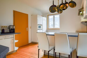 A kitchen with white cabinets, a microwave, and a stove. There are white chairs around a table, and a window with a view. - Holiday flat "Villa Fink attic" with mountain view, private balcony, private terrace and Wi-Fi (Schramberg)