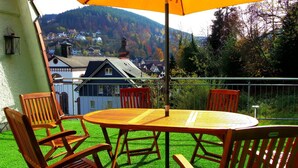 Een balkon met een tafel en stoelen, met uitzicht op huizen en een heuvel op de achtergrond.