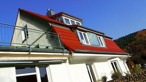A two-story house with a red roof, white walls, and a balcony with a metal railing. - Holiday flat "Villa Fink Obergeschoss" with mountain view, private terrace and wifi. (Schramberg)