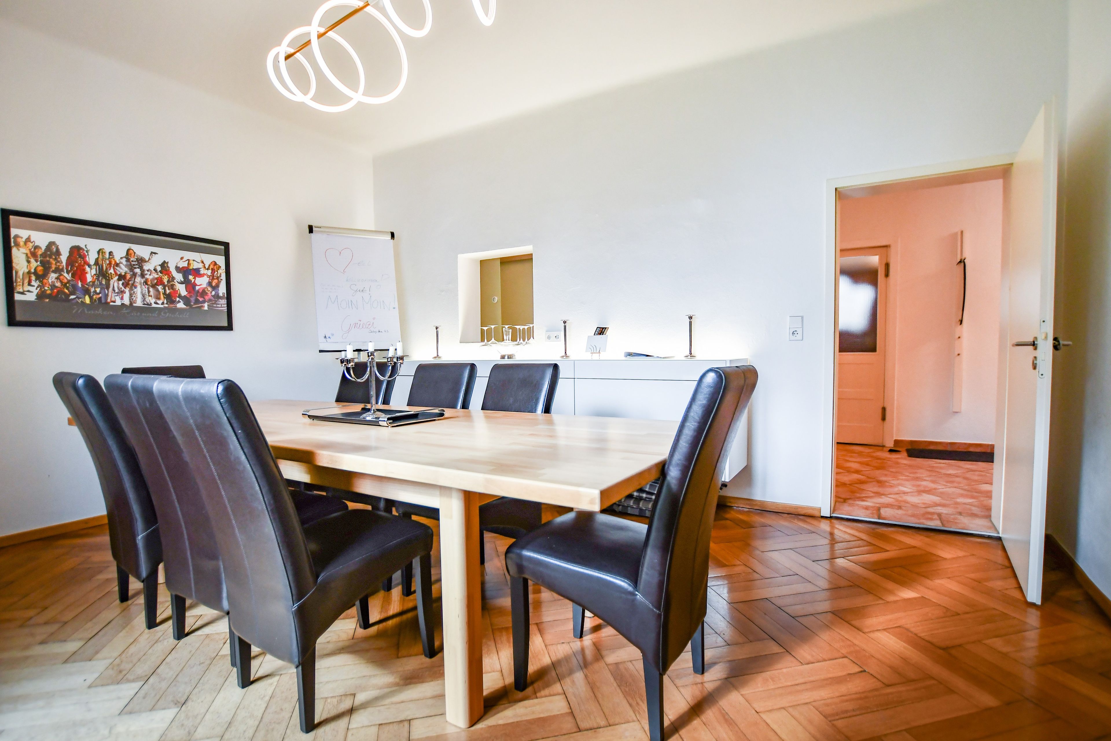 Un salón de conferencias con una mesa de madera, sillas negras, una pizarra y un cuadro en la pared.