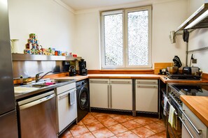 Eine kleine Küche mit Spülmaschine, Kaffeemaschine und einem Fenster mit Blick auf eine Steinmauer.
