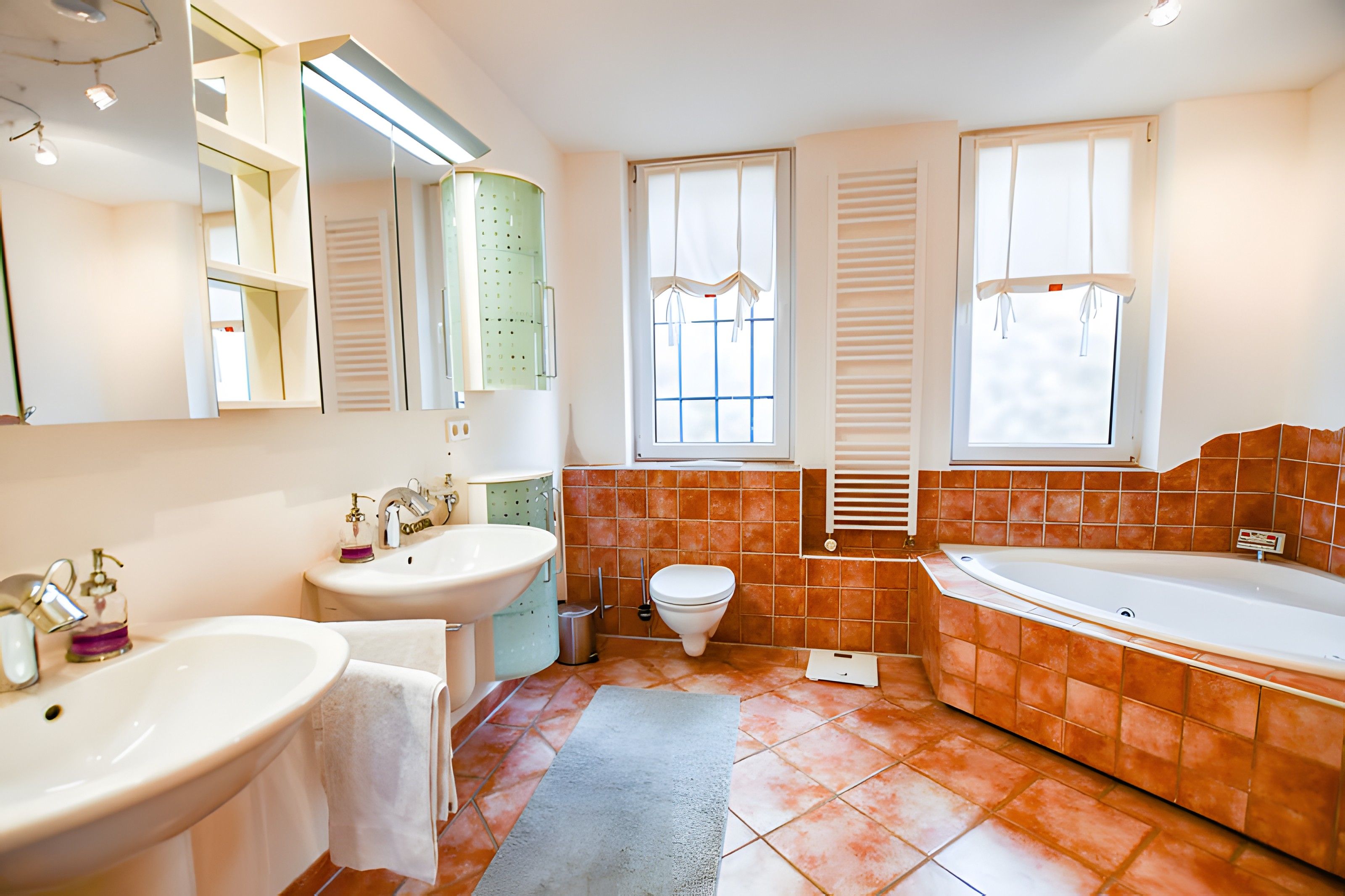 Ein Badezimmer mit einer Badewanne, zwei Waschbecken, einer Toilette und einem Fenster mit Jalousien.