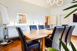 Een moderne eetruimte met een houten tafel en zwarte leren stoelen, een whiteboard met handgeschreven aantekeningen, en een keuken met een spiegel en aanrecht.