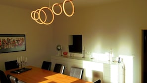 A dining area with a wooden table, chairs, a pendant light, a framed picture, and a kitchen area with a microwave. - Holiday flat "Villa Fink Obergeschoss" with mountain view, private terrace and wifi. (Schramberg)