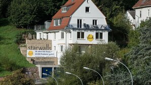 Un immeuble de deux étages doté d’un balcon, entouré de verdure.