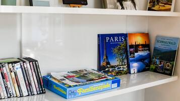 Ein Bücherregal mit verschiedenen Büchern und DVDs, eine kleine Staffelei mit einem Gemälde und zwei Lautsprecherregale.
