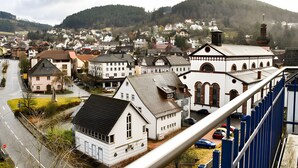 Une ville avec une église imposante, une rue bordée de voitures garées et une colline en arrière-plan.