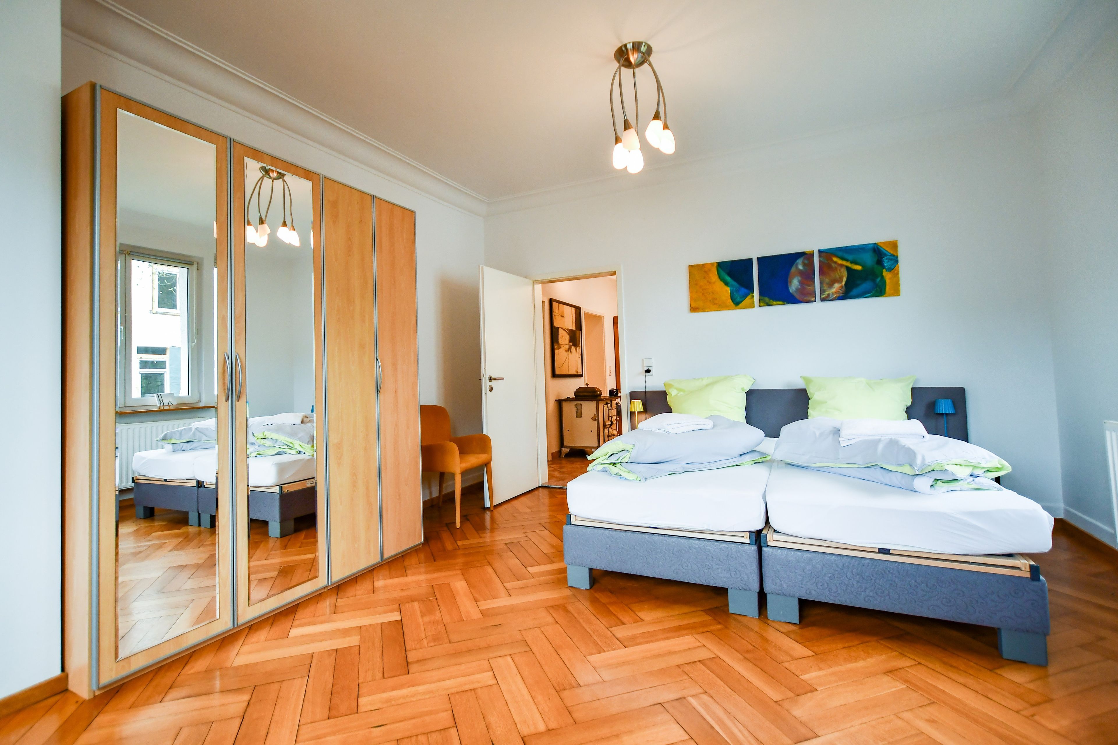 Ein modernes Schlafzimmer mit großem Kleiderschrank, einem Doppelbett und einem Fischgrätparkett.