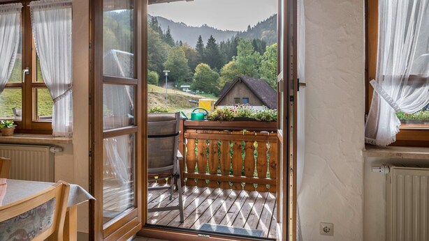 A wooden deck with a chair and a table, a view of a house and mountains, and a door leading to the deck.
