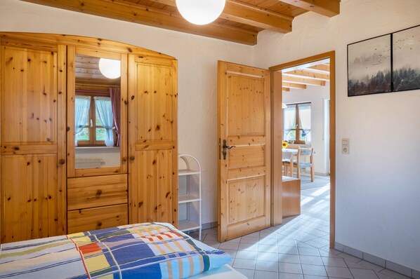 A bedroom with wooden wardrobes, a bed with a colorful quilt, and a view of a dining area.