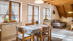 A cozy room with a dining table, chairs, a sofa, and a window with curtains.