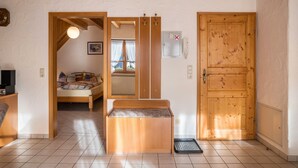 A room with a bed, a bench, a wooden door, and a small window.