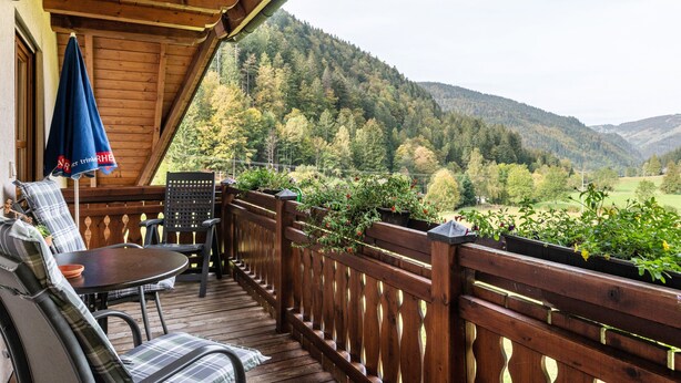 A wooden deck with outdoor seating, a view of a forested valley, and a wooden railing. - Apartment Afterglow (Oberried-St. Wilhelm)