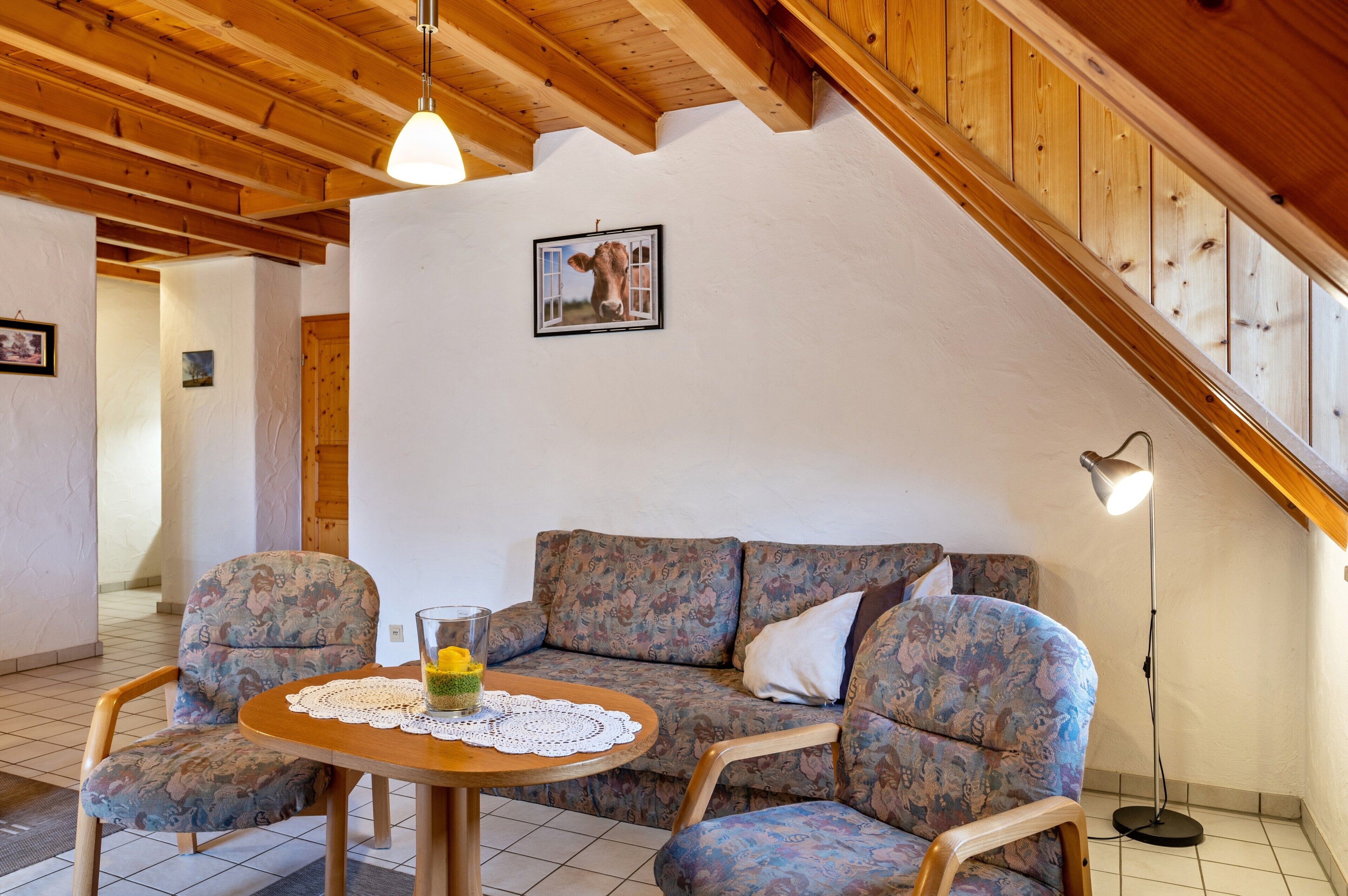 Una habitación acogedora con techo de madera, un sofá, una mesa con un centro de mesa de cristal y un cuadro en la pared.