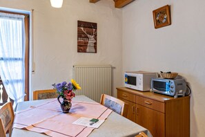 Ein Essbereich mit einem Tisch für zwei Personen, einer Blumenvase, einem Holzkorpus mit einer Mikrowelle und einer Wanduhr.