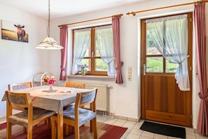 A dining area with a table, chairs, a hanging light fixture, and a window with curtains. - Apartment Wiesengrund (Oberried-St. Wilhelm)