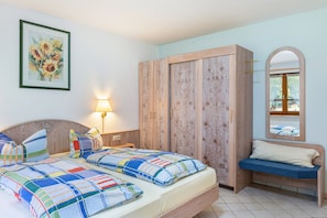 A bedroom with two beds, a wooden wardrobe, a bench, a mirror, and a wall-mounted lamp. - Apartment Wiesengrund (Oberried-St. Wilhelm)