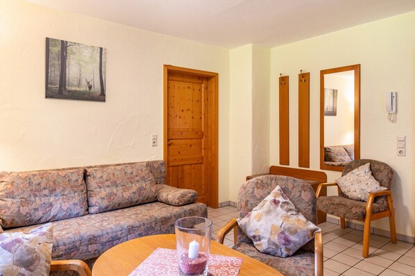 Un salon avec un canapé, des fauteuils, une porte en bois, un miroir et un tableau accroché au mur.