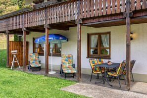 Une terrasse extérieure avec une table et des chaises, une pergola en bois et un parasol bleu.