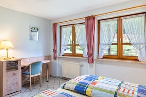 Une chambre à coucher avec un lit, un bureau, une chaise et deux fenêtres avec des rideaux.