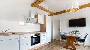 Een moderne keuken met witte kasten, een houten eettafel en een flatscreen televisie aan de muur.