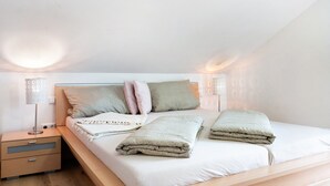 Een keurig opgemaakt bed met kussens en een dekbed, een nachtkastje met een lamp, en een wandlamp.