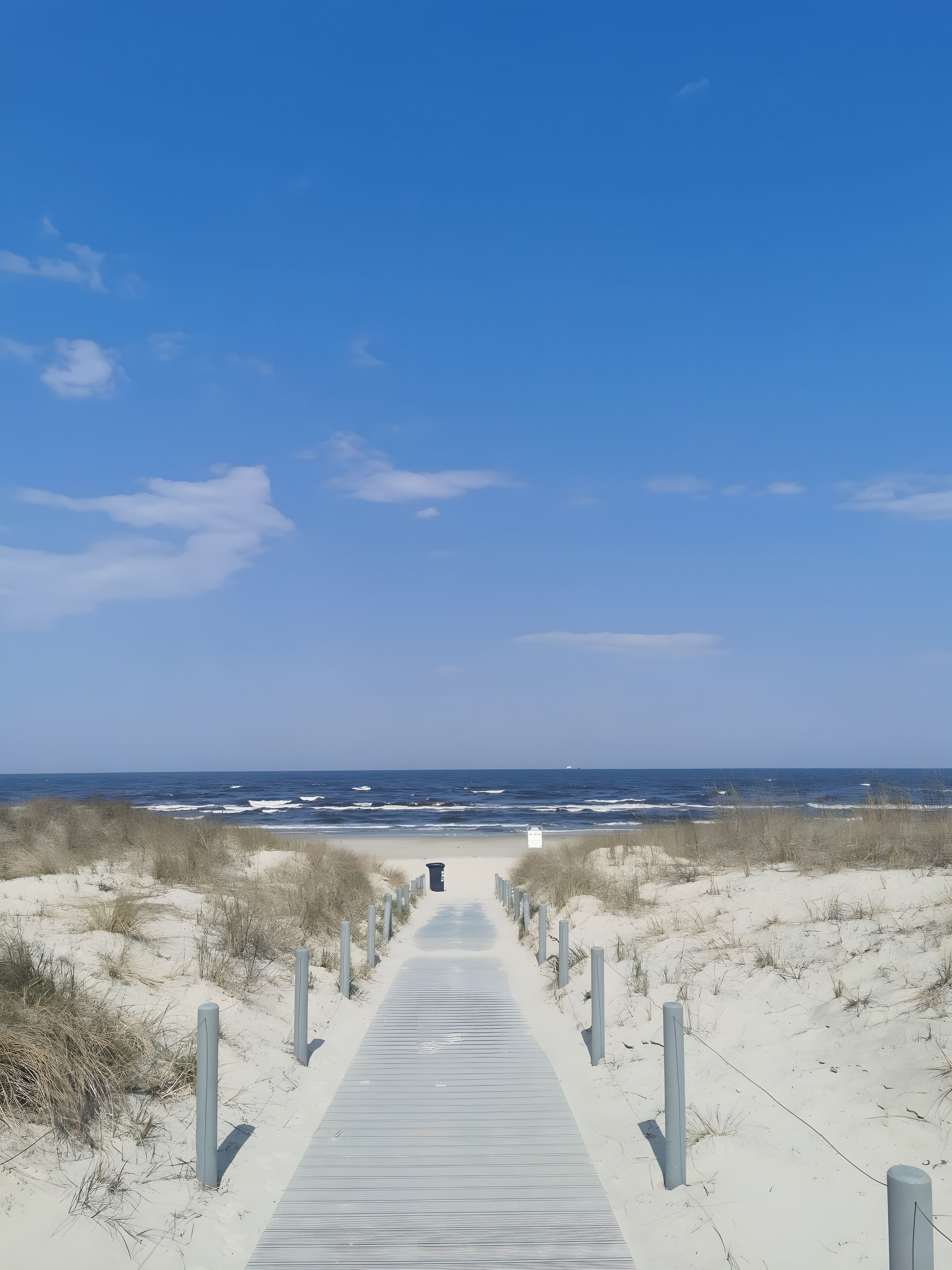 Ein hölzerner Steg führt zum Strand, begleitet von Dünen rechts und links.